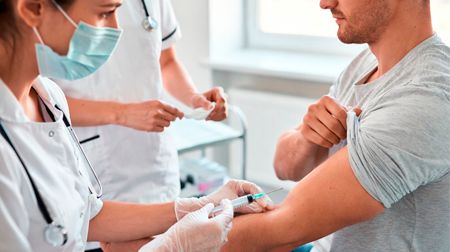 Медсестра в маске и перчатках делает инъекцию в плечо пациента